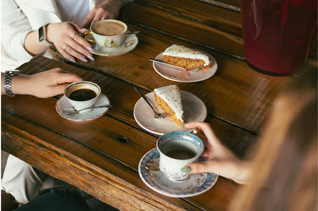 Closeup of Women Sitting at a Wooden Table with Carrot Cakes and Hot Drinks