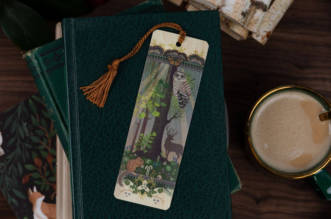 Dark green vintage books topped with a woodland-themed bookmark beside a warm cup of chai, creating a cozy hygge reading scene.