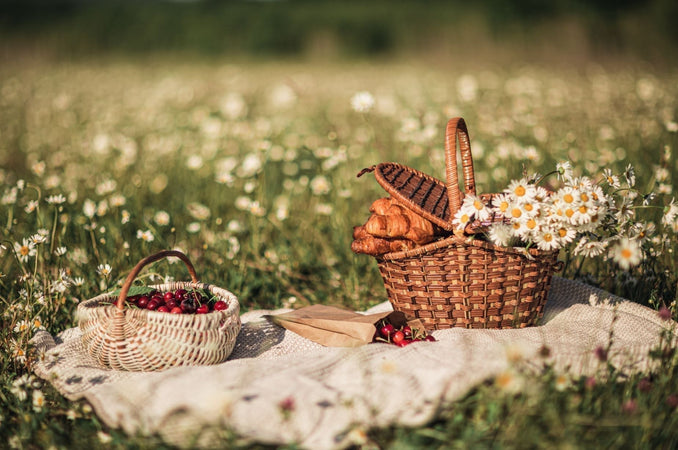 Straw Picnic Baskets filled with berries, flowers and croissants in an outdoor setting.