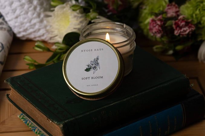 Soft Bloom candle glowing on a stack of vintage books, surrounded by fresh flowers.
