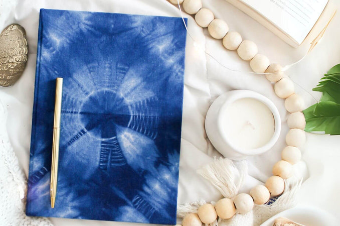 Flat lay of Handmade Blue Tie Dye Hardcover Journal with a candle and wooden beads