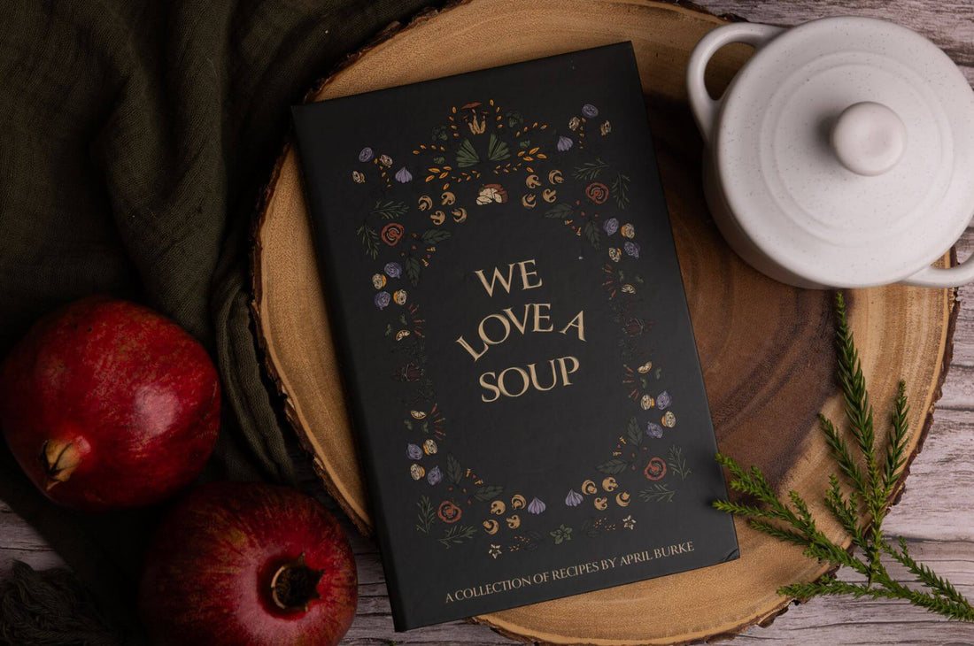Fall soup cookbook styled with a white ceramic pot, pomegranates, greenery, and warm natural textures for a cozy weekly soup tradition.