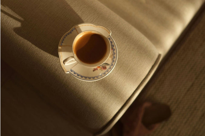 Warm cup of tea in a vintage teacup resting on a chair in soft morning sunlight.