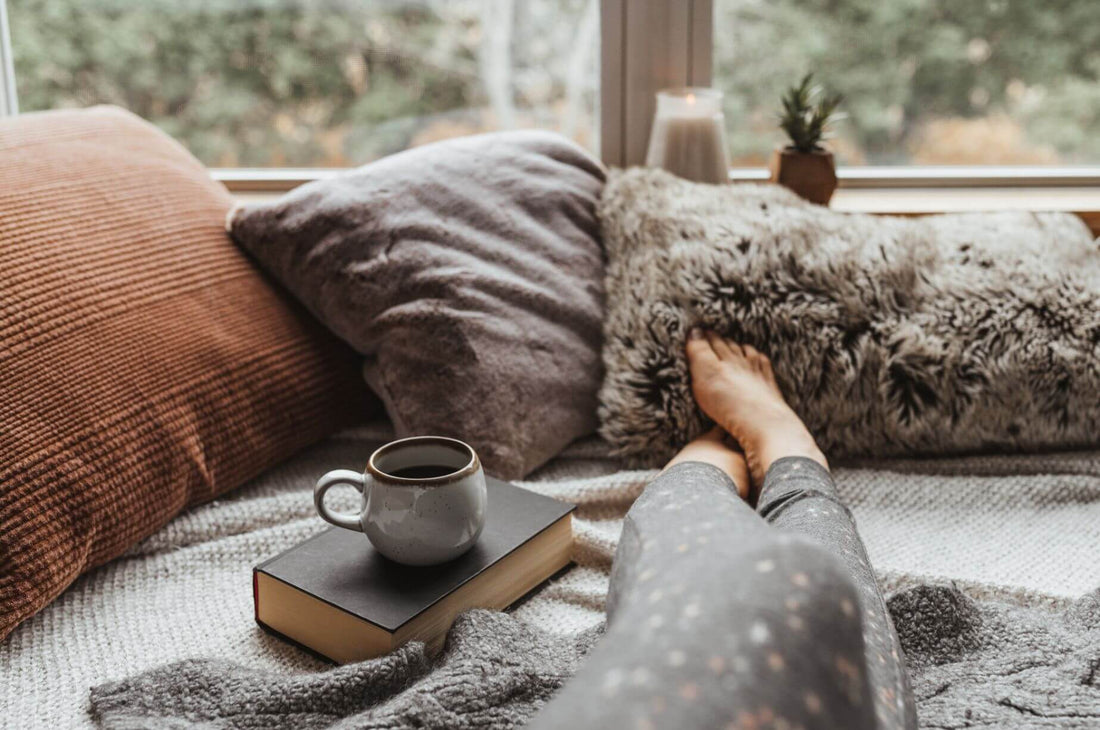 Woman resting on a couch with a warm mug and book, a cozy søndagshygge Sunday at home