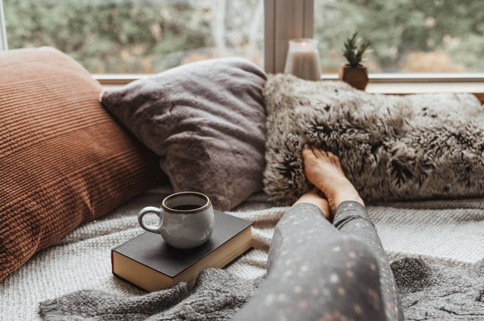 Woman resting on a couch with a warm mug and book, a cozy søndagshygge Sunday at home