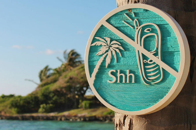 Round wooden plaque with a palm tree and a line crossed over a picture of a cell phone and the word "shh"