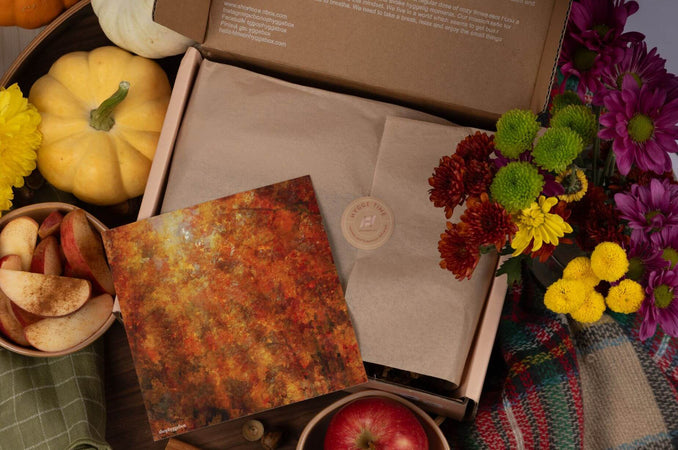 September Hygge Box styled with autumn flowers, mini pumpkins, sliced apples, an olive napkin, and a warm-toned fall art print.