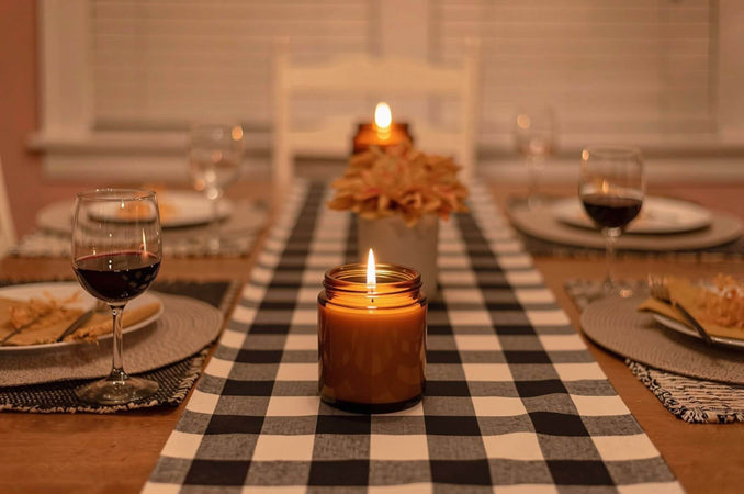 Cozy fall dinner table with a glowing candle, wine glasses, autumn flowers, and a black-and-white checkered runner.