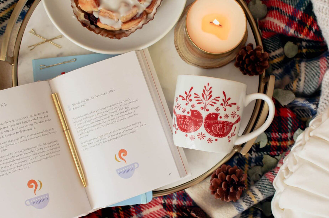 A hygge lifestyle flat lay with book, candle, cup and pastry.