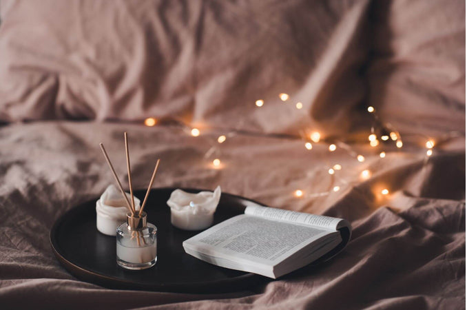 The Joy of Disconnecting with Hygge - cozy bed with string lights, candles and an open book
