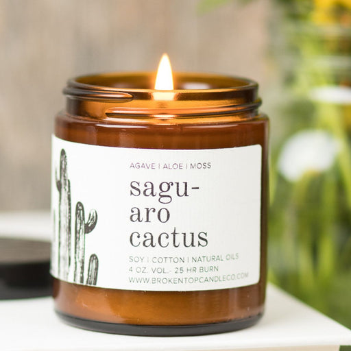 An amber jar candle labeled Saguaro Cactus against a blurred background.
