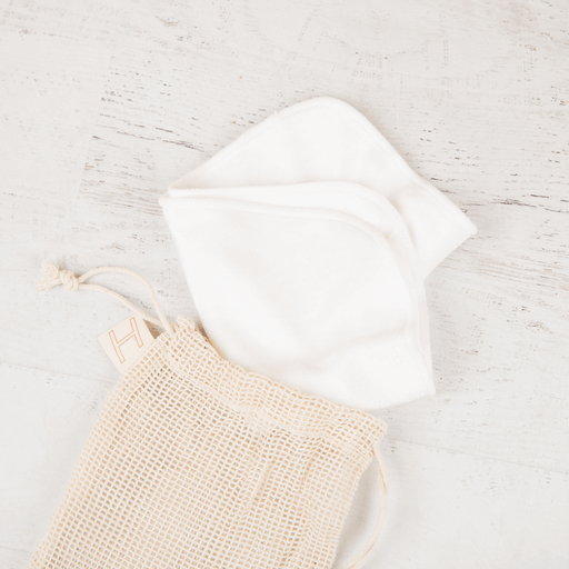 White bamboo face towel and beige mesh travel pouch on a light gray textured surface.