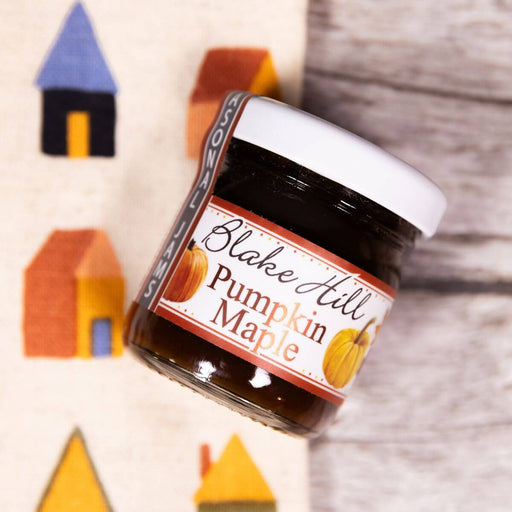 Jar of Blake Hill Pumpkin Maple on a textured surface with colorful houses on a dish towel in the background