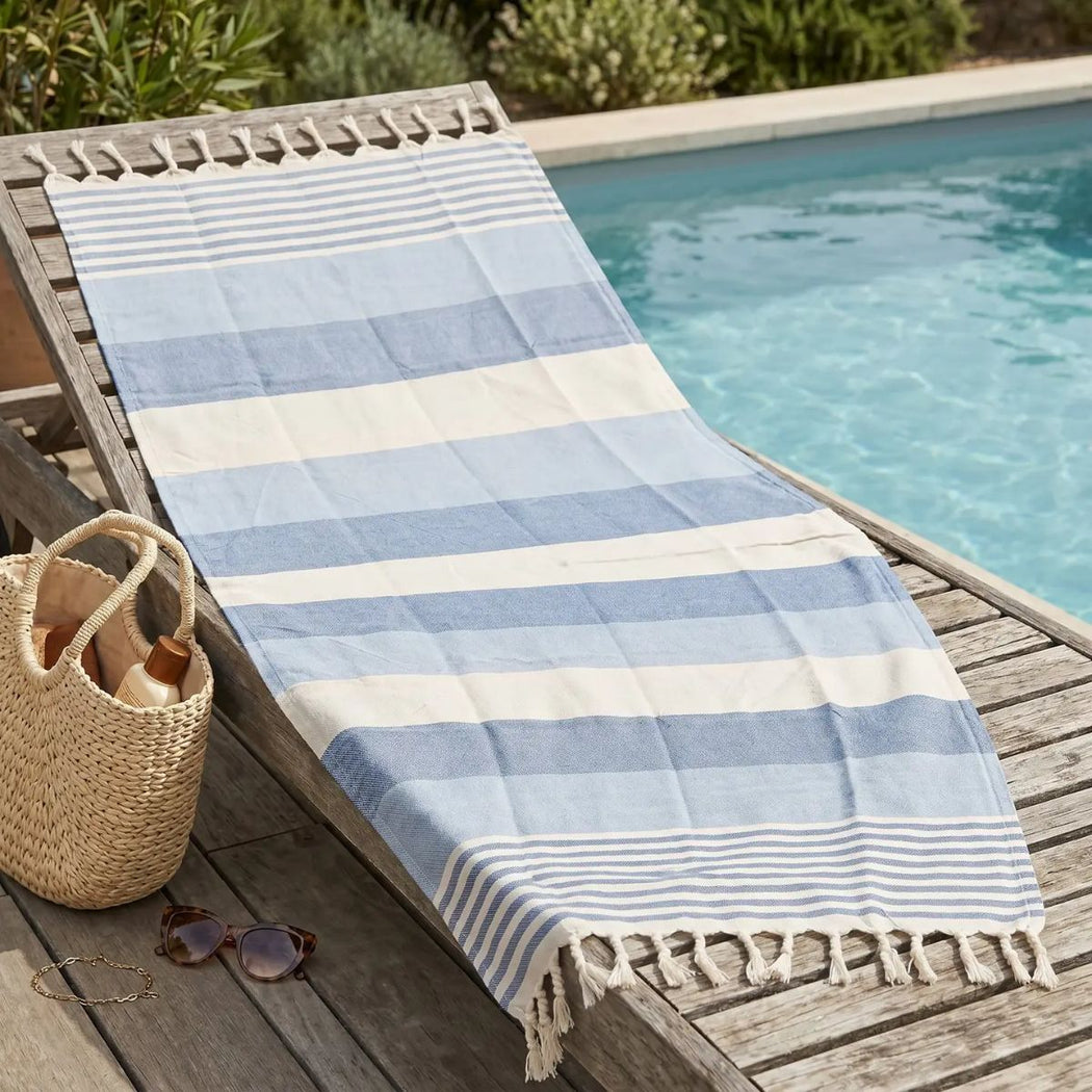 Blue and white striped towel on a wooden lounge chair by a poolside.