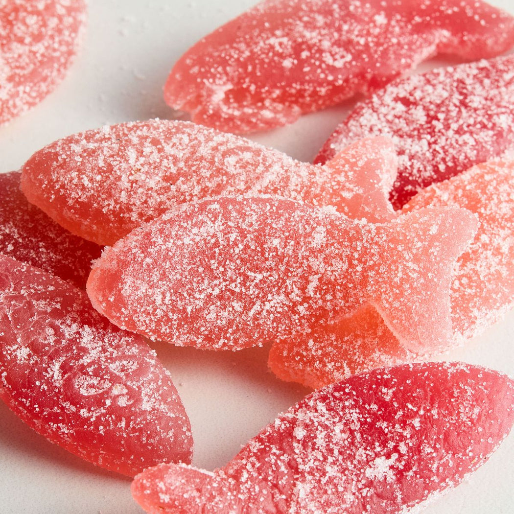 Close-up of several Bon Bon Sour Wild Strawberry pink fish-shaped gummy candies coated with white sugar powder on a white background.
