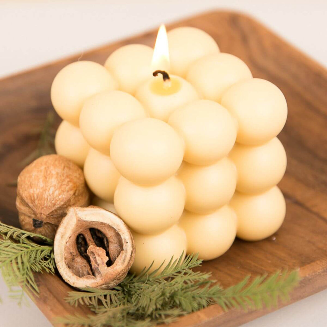 Bubble Cube Candle on a wooden board with nuts and greenery.