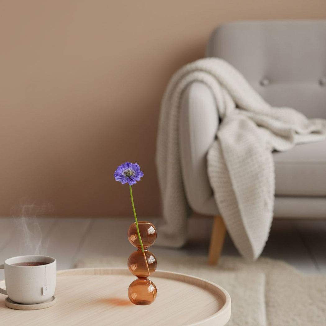 Small vase with a purple flower on a wooden tray in a cozy living room.
