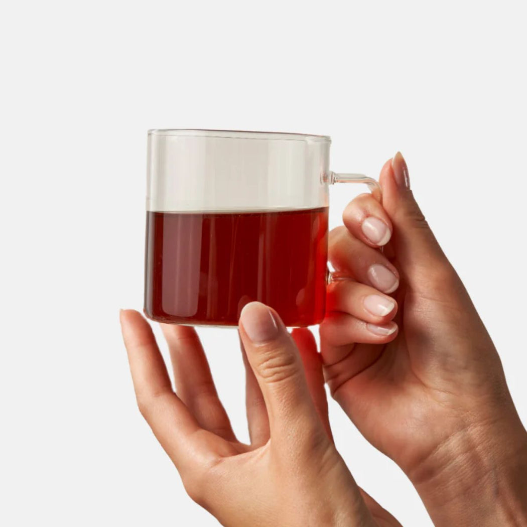 Hand holding a clear mug with red colored chai tea against a white background