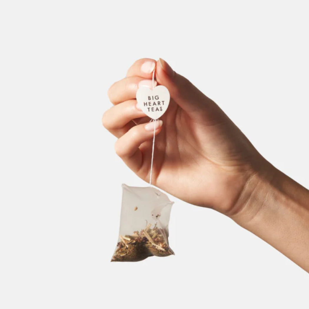 Hand holding a tea bag labeled 'Big Heart Tea' against a white background