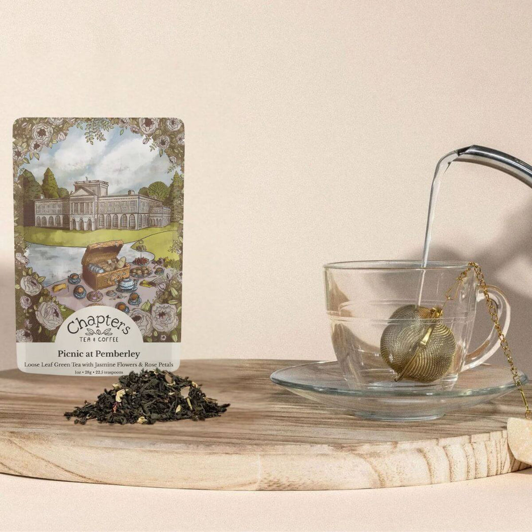 Tea packaging, loose tea leaves, and a glass teacup with a teabag on a wooden surface.