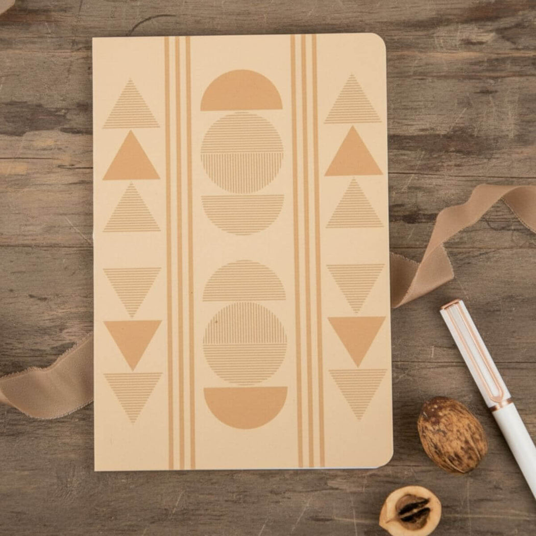 Notebook with geometric patterns on a wooden surface with a pen and nuts.