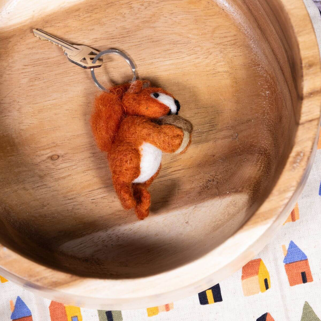 Felted squirrel keychain on a wooden surface.