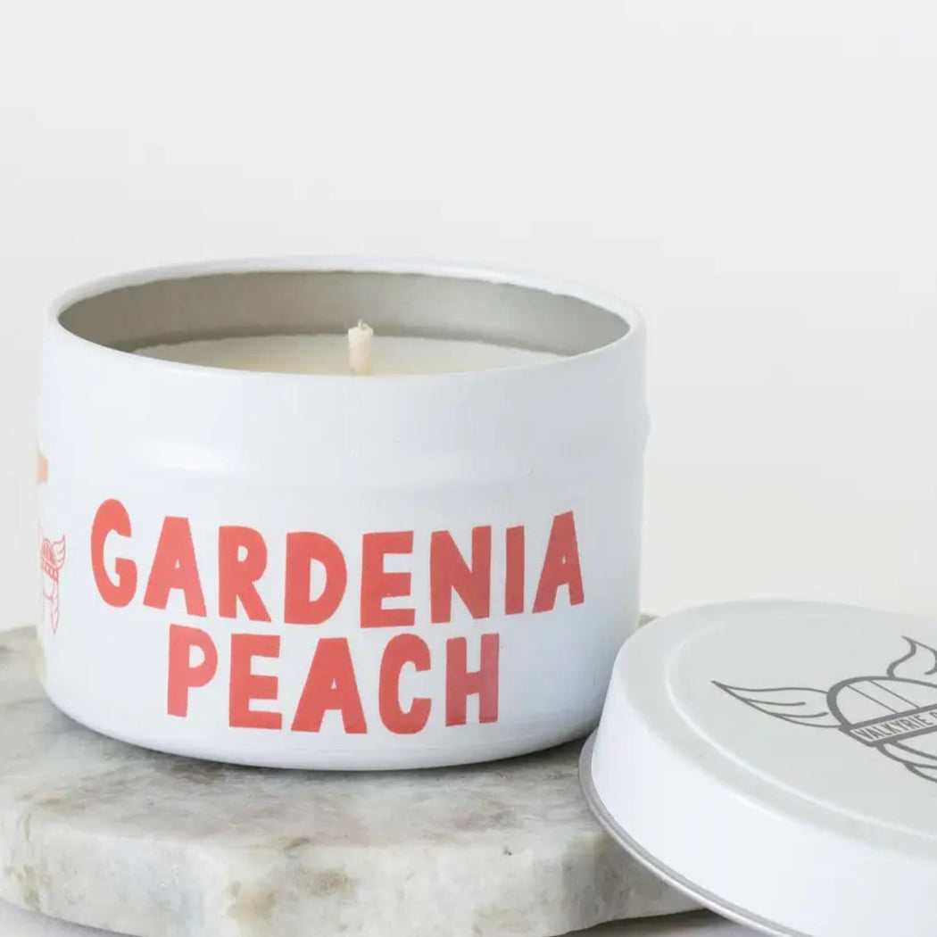Candle in a white container with 'Gardenia Peach' text on a marble surface.