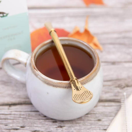 Gray ceramic mug with a gold filter straw on the cup of tea on a wooden surface.