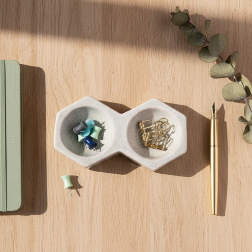 Ceramic two-compartment organizer with office supplies on a wooden surface with eucalyptus leaves.