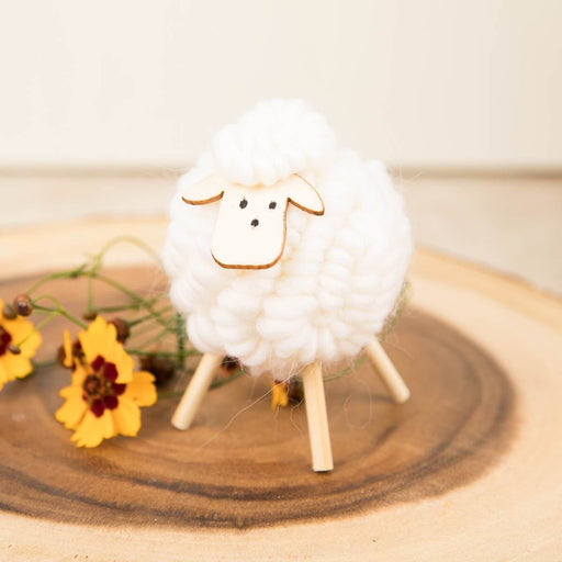 White fluffy sheep figurine on a wooden surface with yellow flowers