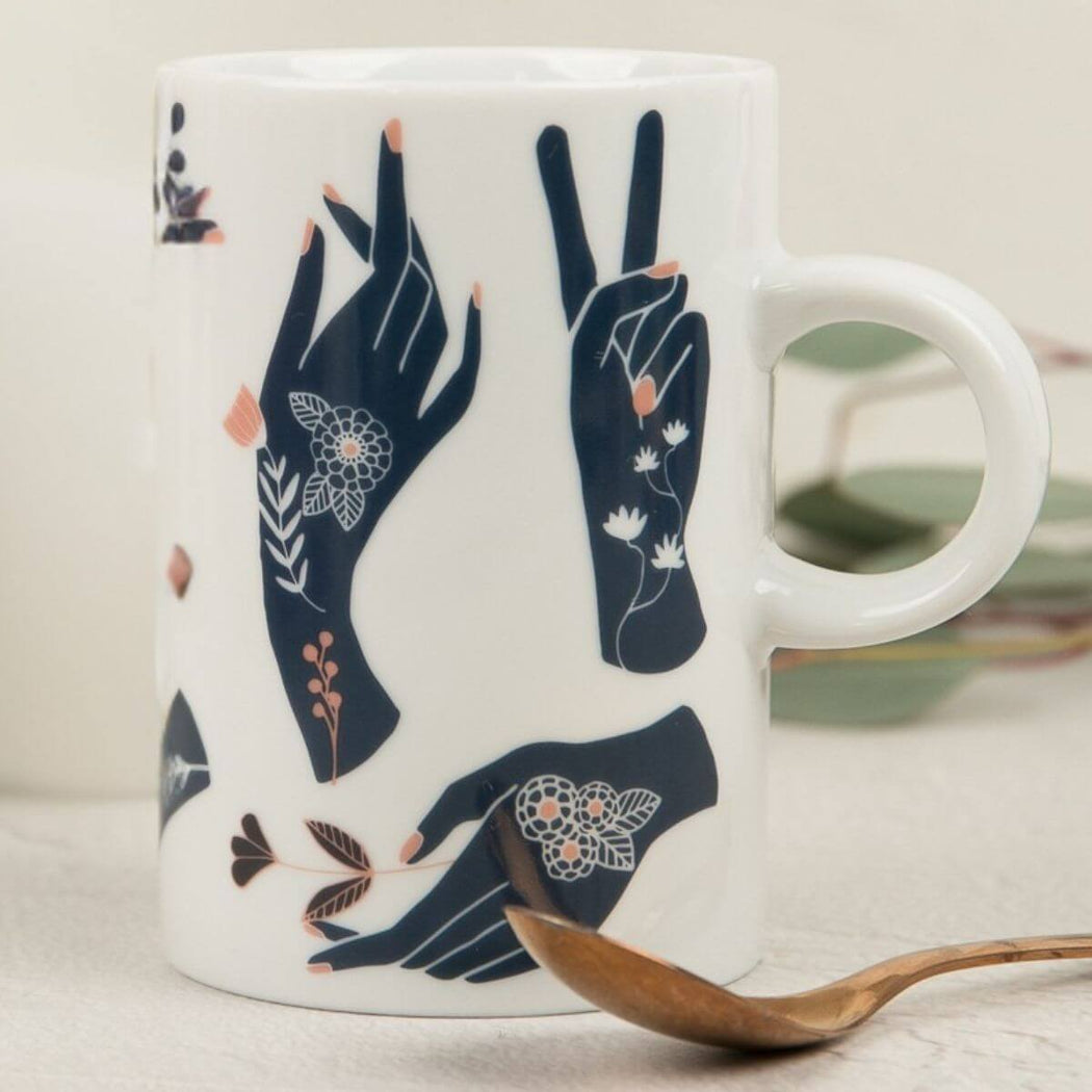 White mug with navy hand illustrations and floral details on a light surface.