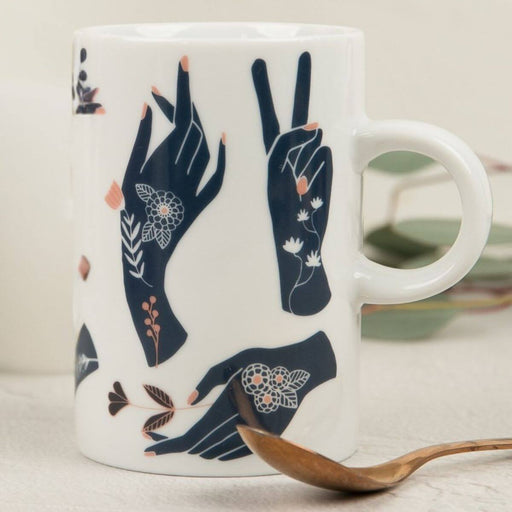 White mug with navy hand illustrations and floral details on a light surface.