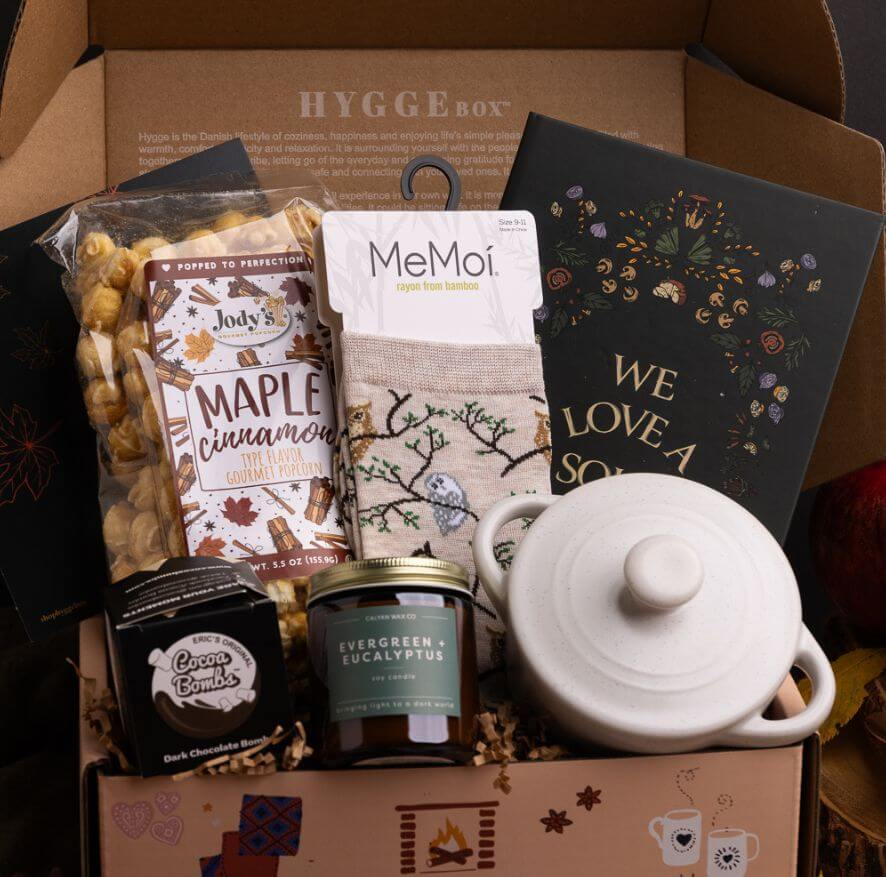 A Hygge Box Subscription Box with various items including a cocotte, candle, socks, and snacks.