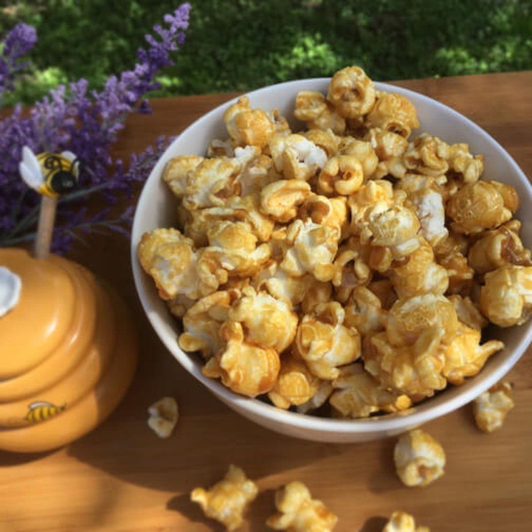 White bowl filled with popcorn on a wooden surface with lavender flowers and a honey jar in the background.