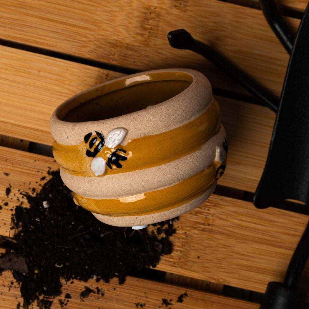 Small ceramic beehive planter pot with soil on a wooden surface