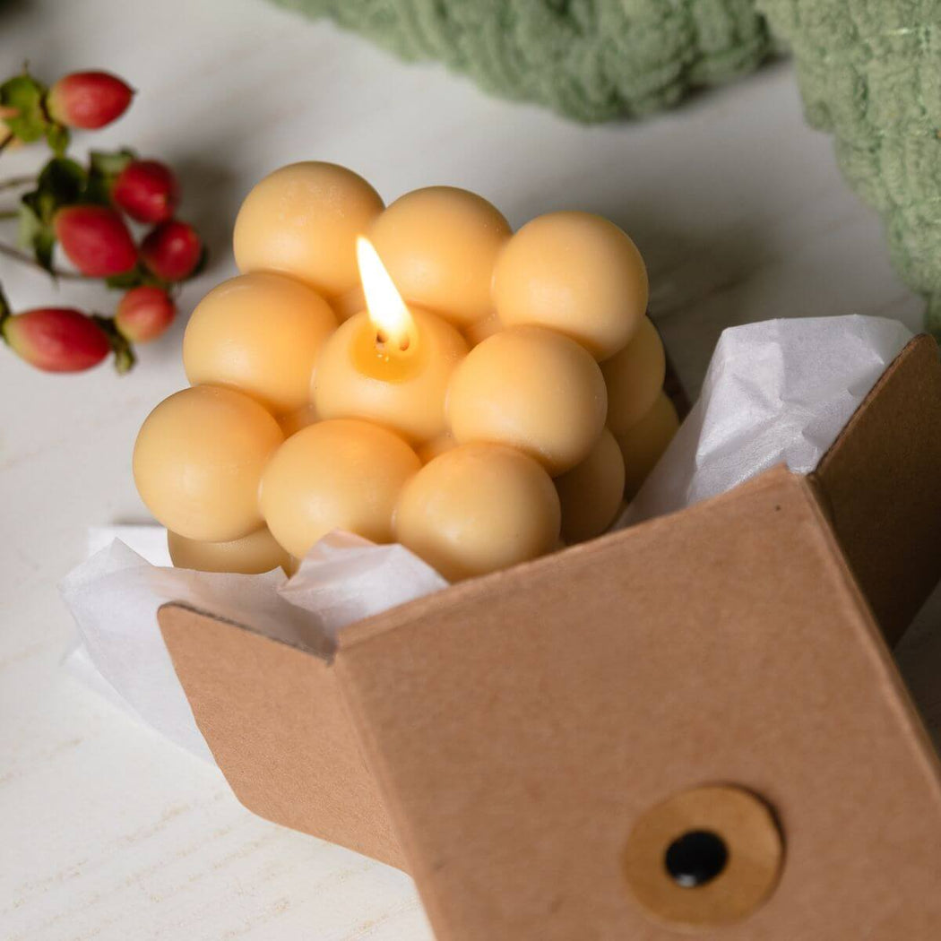 Bubble cube candle in a cardboard box with berries and greenery in the background.