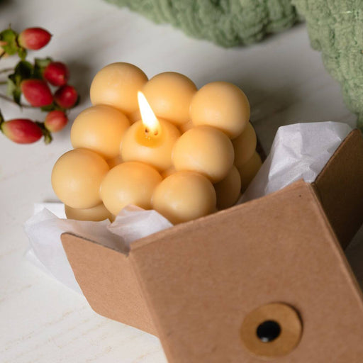Bubble cube candle in a cardboard box with berries and greenery in the background.