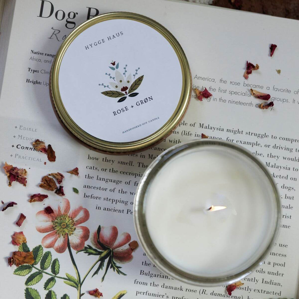 Candle in a glass jar with a decorative lid on an open book with floral illustrations