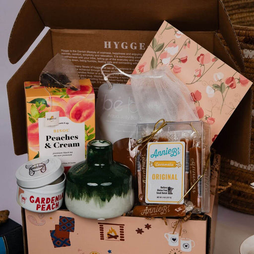 Hygge Box Gift with candles, tea, and other items on a wooden surface