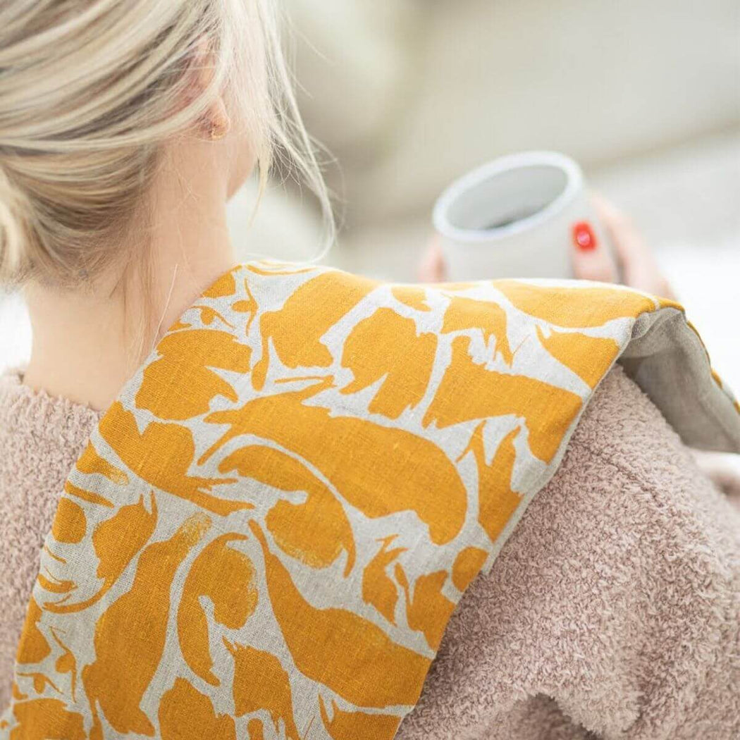 Woman wearing yellow linen wheat wrap heat pack on shoulders for neck and shoulder heat therapy