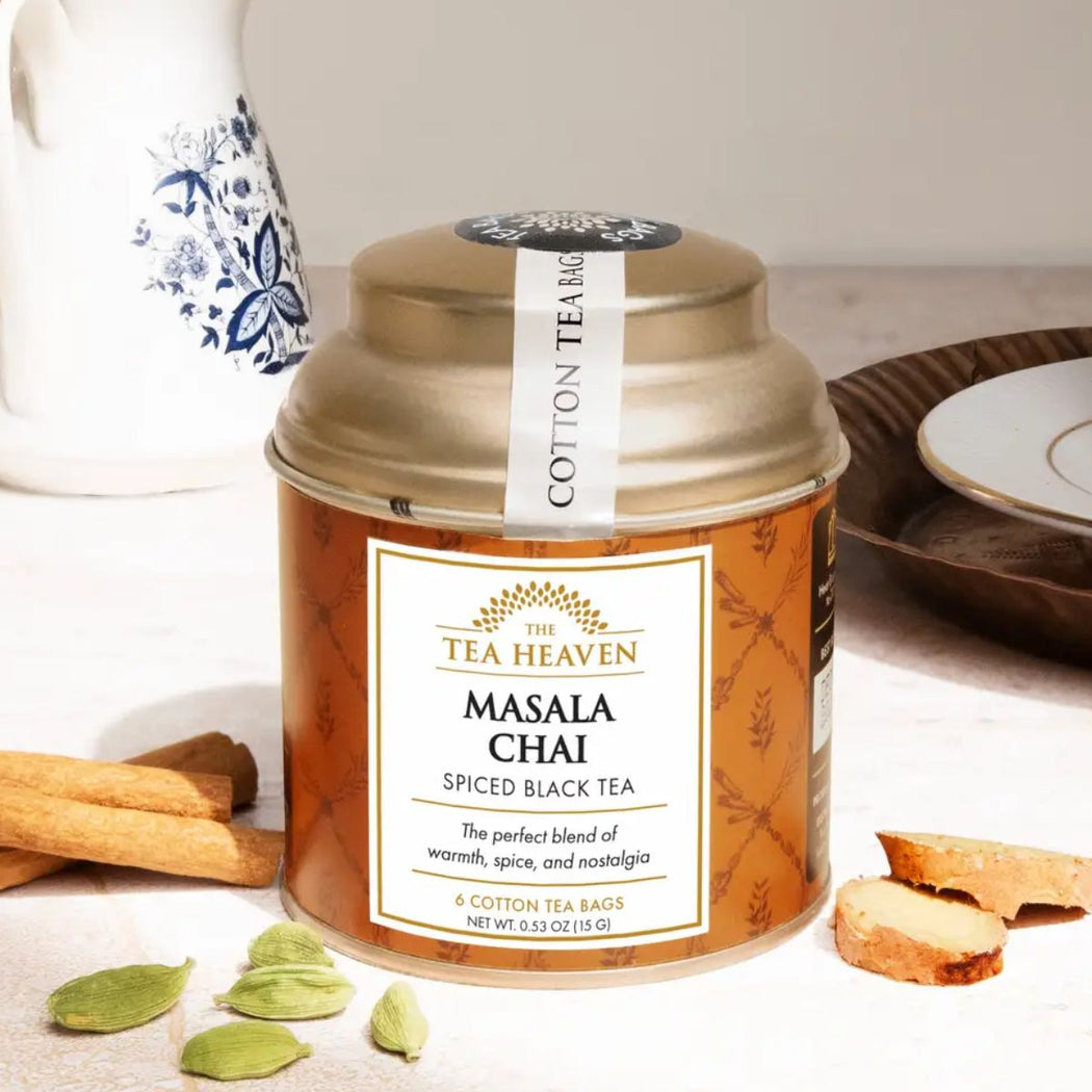 Tea canister labeled 'The Tea Heaven Masala Chai' on a table with cinnamon sticks and cardamom pods.