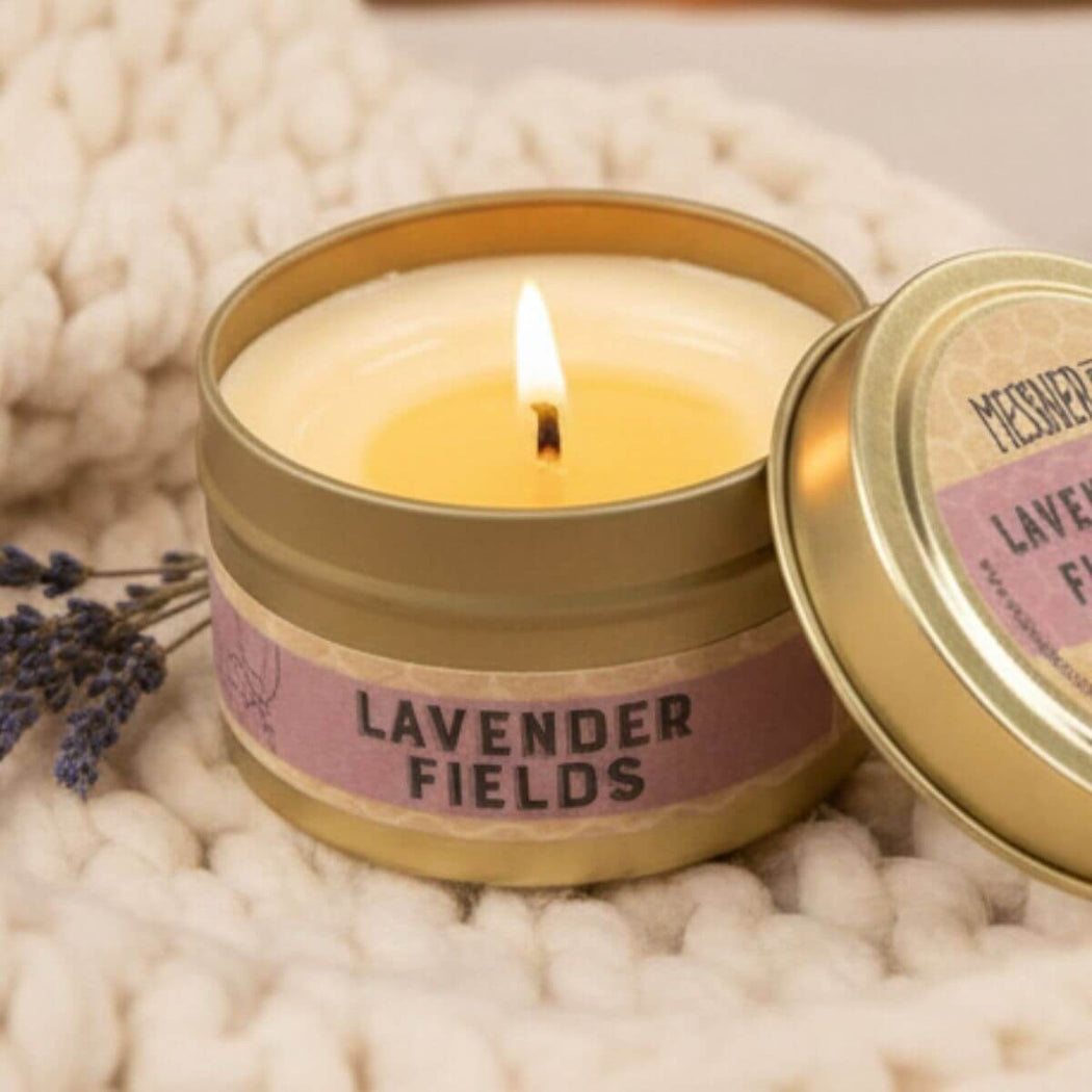 Lavender Fields Scented Candle in Gold Metal Tin laying on top of a cozy knit with a sprig of lavender