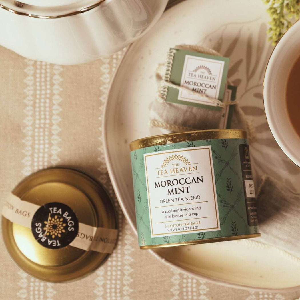 Tea Heaven Moroccan Mint green tea blend packaging on a table with a teacup and saucer.