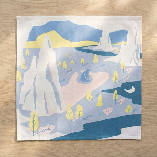 Decorative 25"x25" towel with a mountain and landscape design on a wooden surface