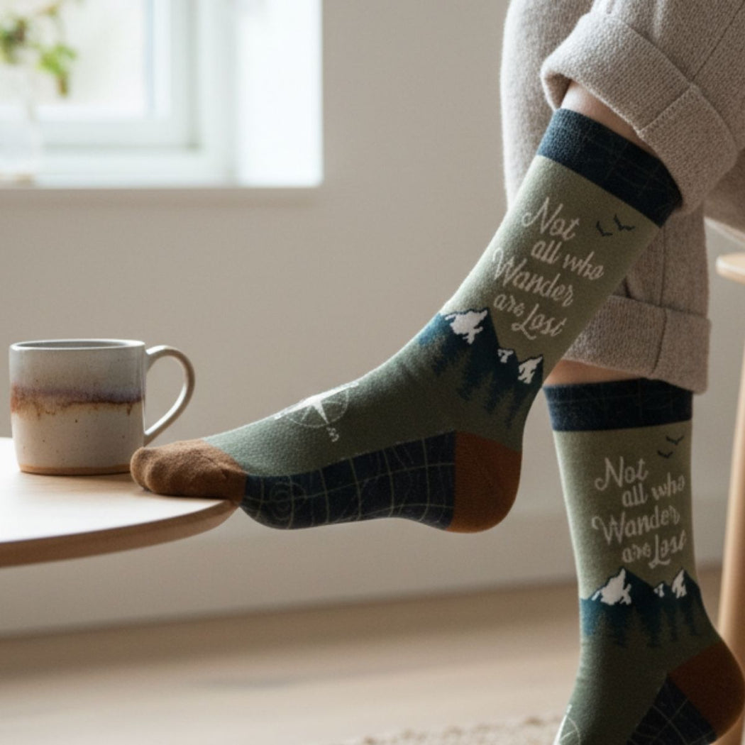 Person wearing socks with text and bird designs, sitting by a window with a mug on a table.