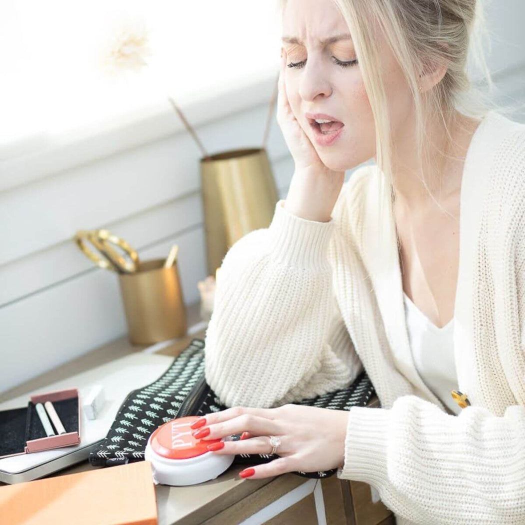 Woman using a PYT button on a desk with a white wall background