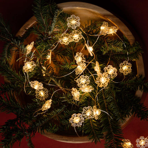 Decorative string lights with snowflake designs in a bowl surrounded by evergreen.