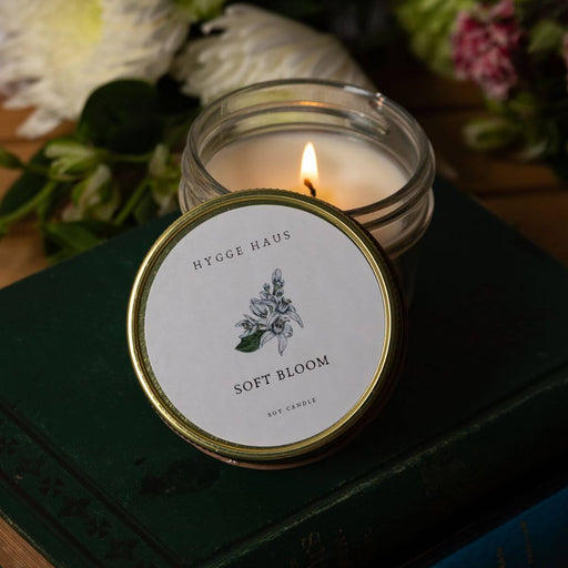 Candle in a glass jar with a visible label on a dark surface with flowers in the background