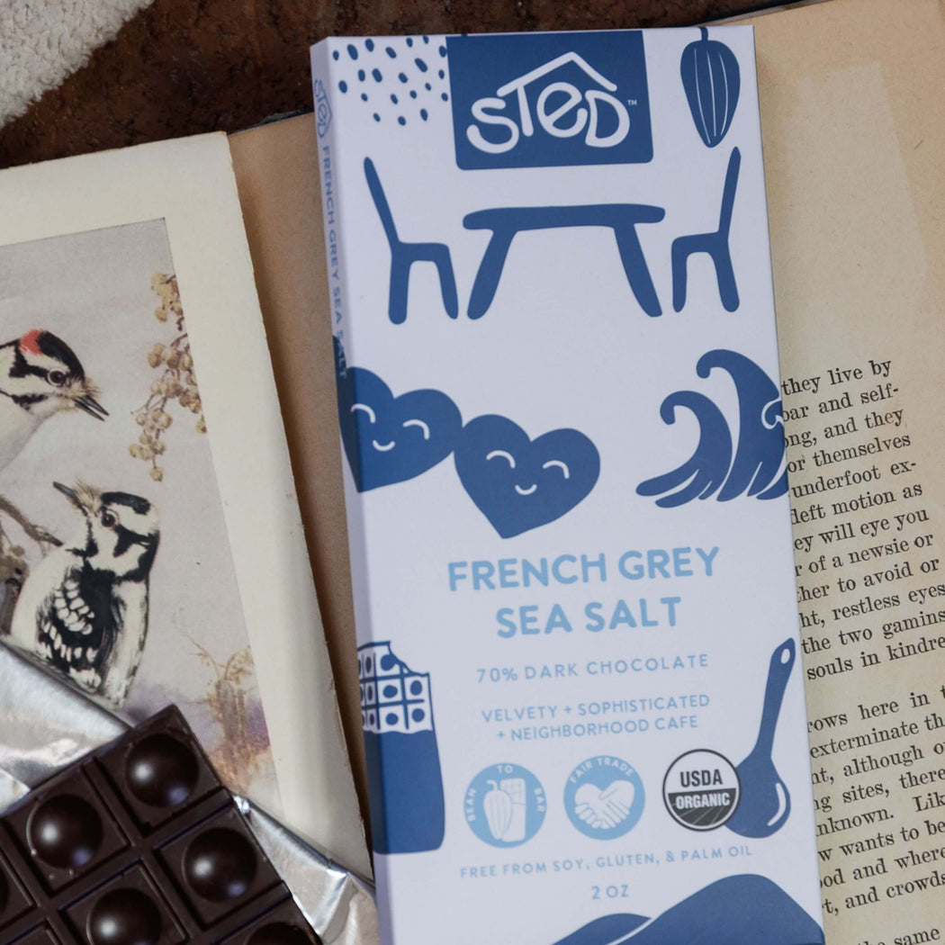 STED French Grey Sea Salt chocolate bar on a surface with a book and chocolate pieces.