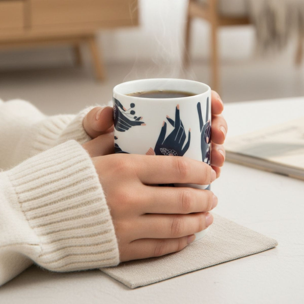 Person holding a mug with floral and hand design on a light surface